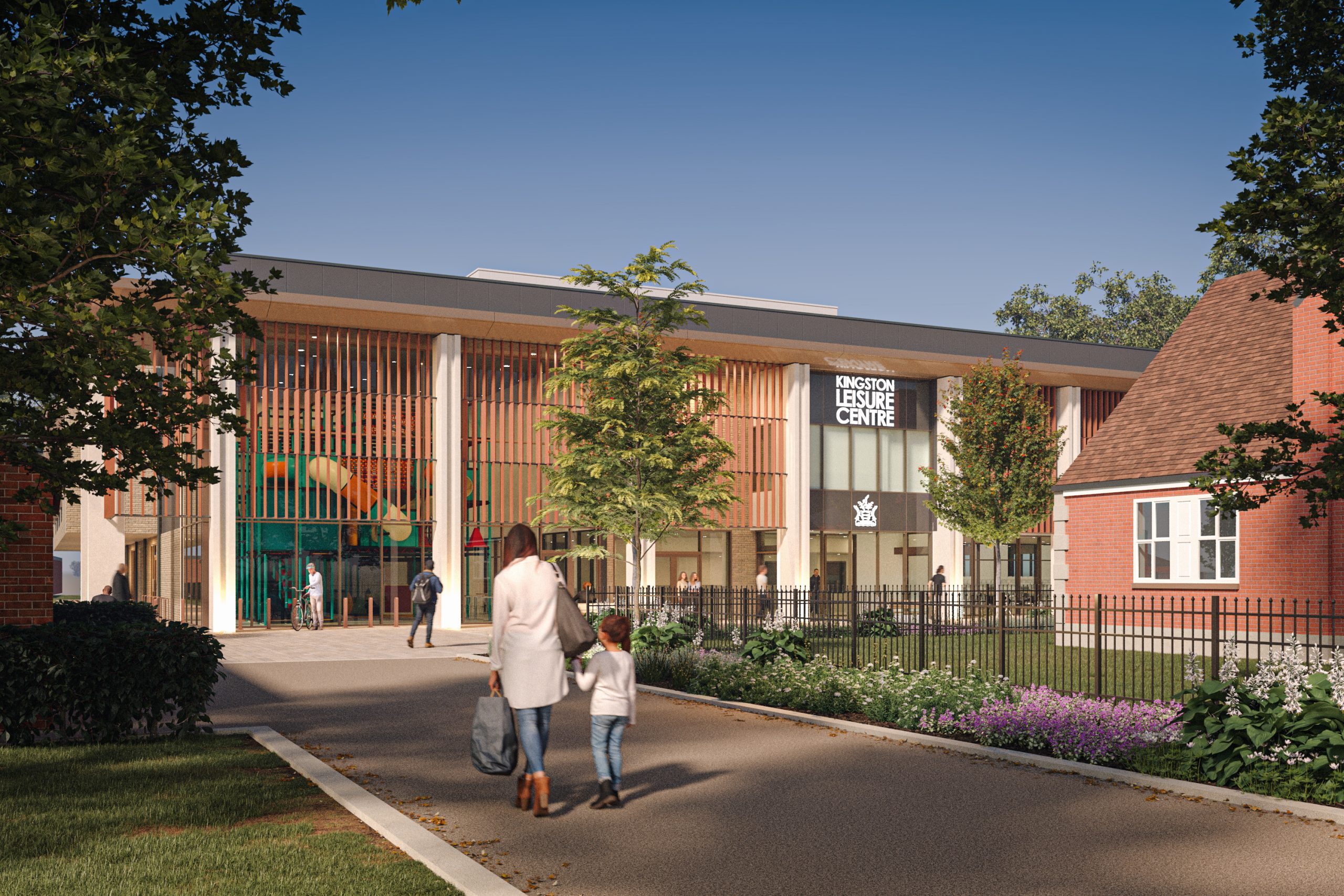 Image showing a wide pathway leading to a 2 storey building with planting and trees either side. A mother and child are walking hand in hand towards a building that has a glass front with large columns.