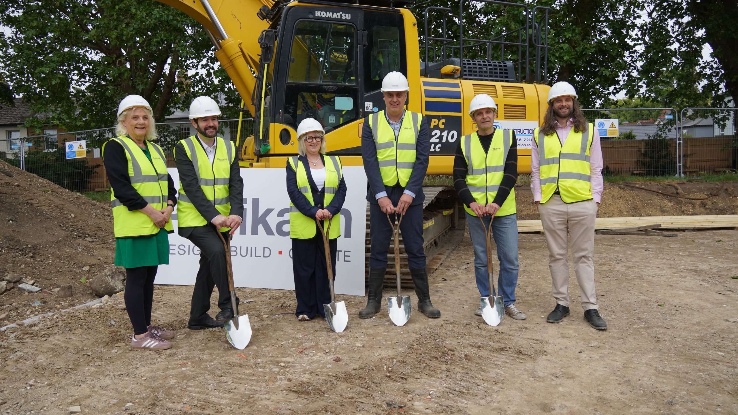 Kingston leisure Centre Construction Image showing six people holding spades, wearing high visibility vests and hard hats, standing in front of construction machinery.